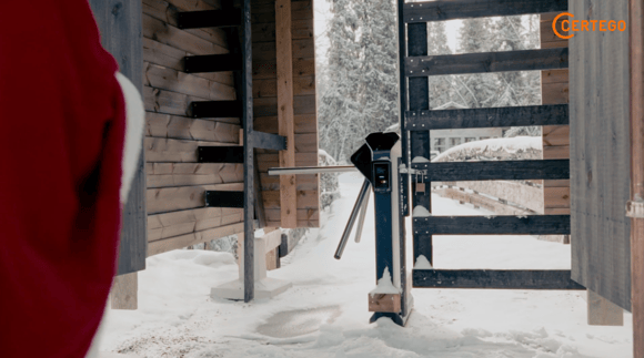 Tonttu kävelee elämyskylän asiakasportin luokse, taustalla näkyy myös riippulukko.