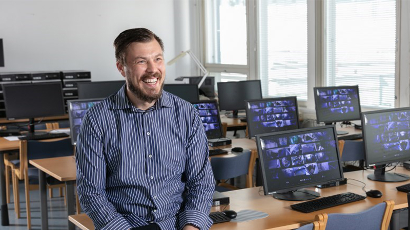 Hymyilevä mies istuu tietokoneiden ääressä